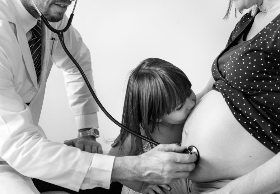 Pregnant woman receiving a prenatal checkup while her daughter kisses her belly