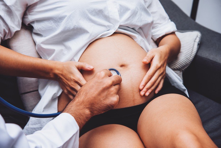 Doctor examining a pregnant woman’s abdomen with a stethoscope during a prenatal checkup.