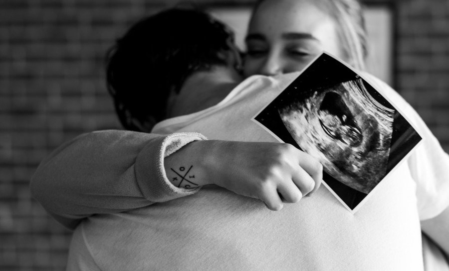 Pregnant woman and her partner embracing while holding an ultrasound image of their baby