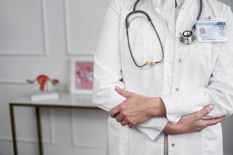 Urologist in a white coat wearing a stethoscope and standing with arms crossed in a medical office.