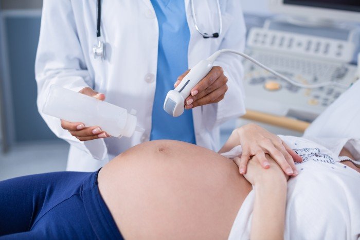 Delivery Specialist performing an ultrasound scan on a pregnant woman’s abdomen during a prenatal checkup.